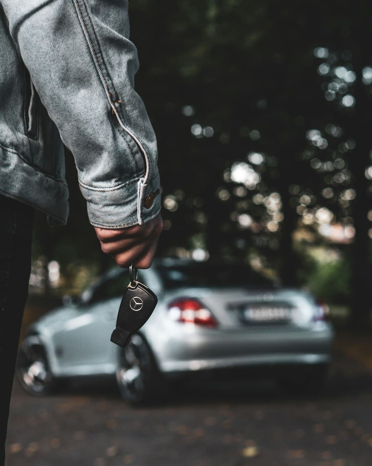 A person holding a car key beside a silver car.